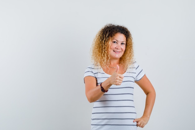 Mooie vrouw die duim in t-shirt toont en er positief uitziet, vooraanzicht.