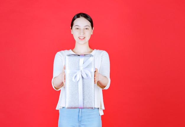 Mooie vrouw die een ingepakte geschenkdoos vasthoudt en op de rode muur staat