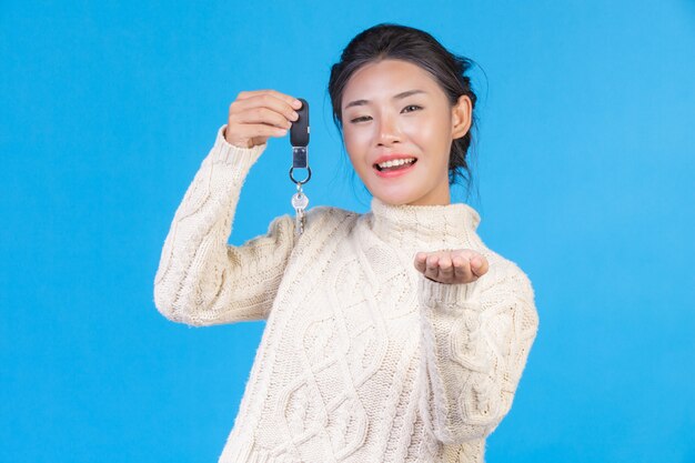 Mooie vrouw die een nieuw wit tapijt met lange mouwen draagt, die een sleutelring in de hand op een blauw houdt. Handel s.