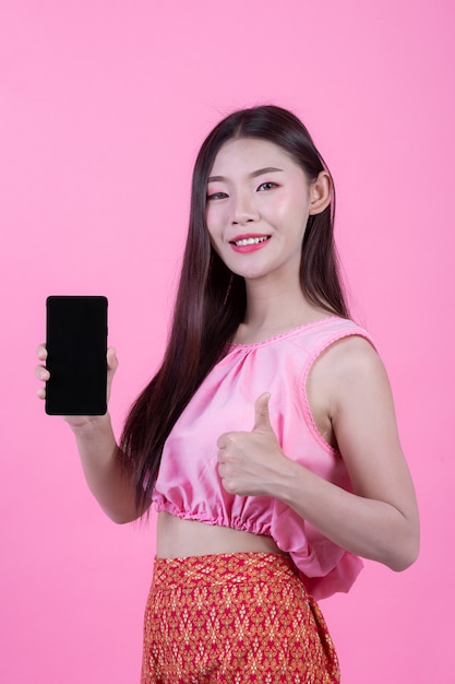 Mooie vrouw die een smartphone op een roze achtergrond houdt.