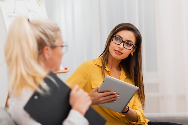 Gratis foto mooie vrouw die een tablet houdt en haar collega bekijkt