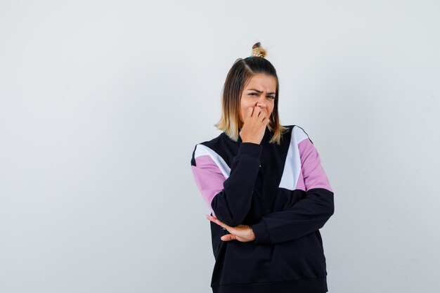 Mooie vrouw die haar hand op de mond houdt in een sweatshirt en er ontevreden uitziet