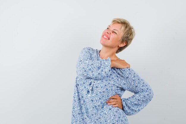 Mooie vrouw die haar schouder in blouse met patroon masseert en er ontspannen uitziet. vooraanzicht.