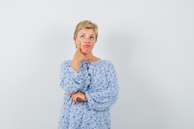 Mooie vrouw die in gedessineerde blouse naar haar oog wijst en verbaasd, vooraanzicht kijkt.