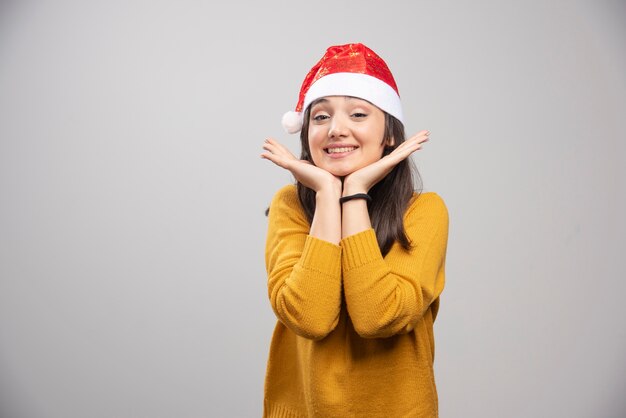 Mooie vrouw die in Kerstmanhoed gelukkig op grijze muur voelt.