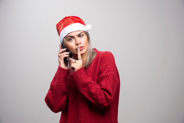 Mooie vrouw die in Kerstmanhoed iemand op telefoon roept.