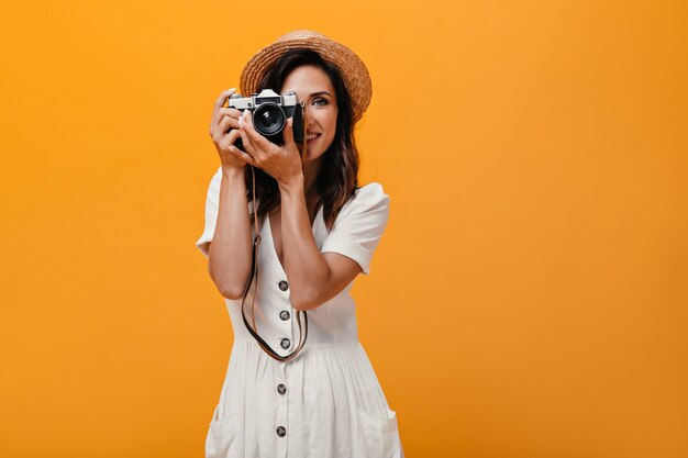 Mooie vrouw die in strohoed retro camera op geïsoleerde achtergrond houdt