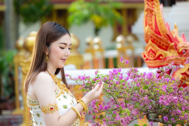 Mooie vrouw die in Thaise traditionele uitrusting en zich bij tempel glimlacht bevindt