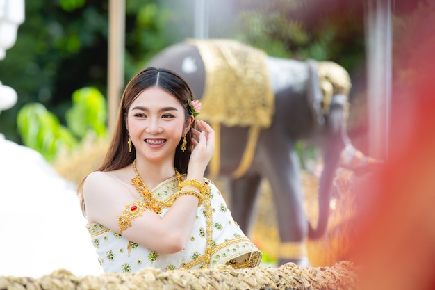 Mooie vrouw die in Thaise traditionele uitrusting en zich bij tempel glimlacht bevindt