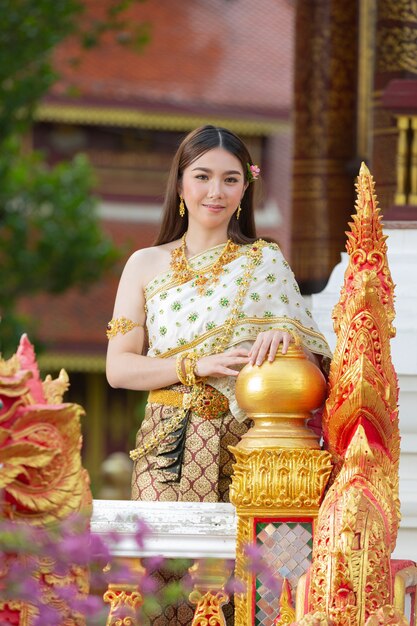 Mooie vrouw die in Thaise traditionele uitrusting en zich bij tempel glimlacht bevindt