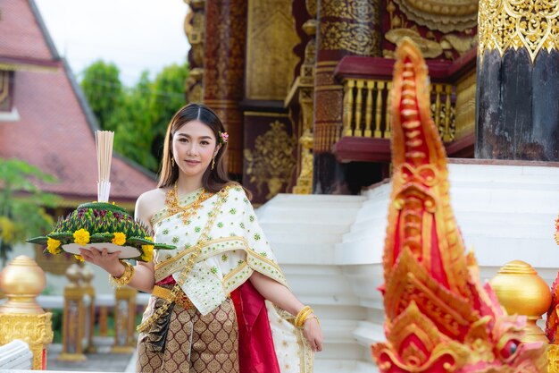 Mooie vrouw die in Thaise traditionele uitrusting en zich bij tempel glimlacht bevindt