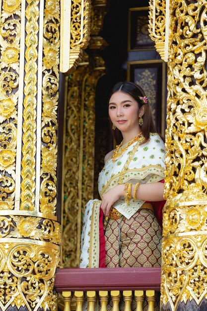 Mooie vrouw die in Thaise traditionele uitrusting en zich bij tempel glimlacht bevindt