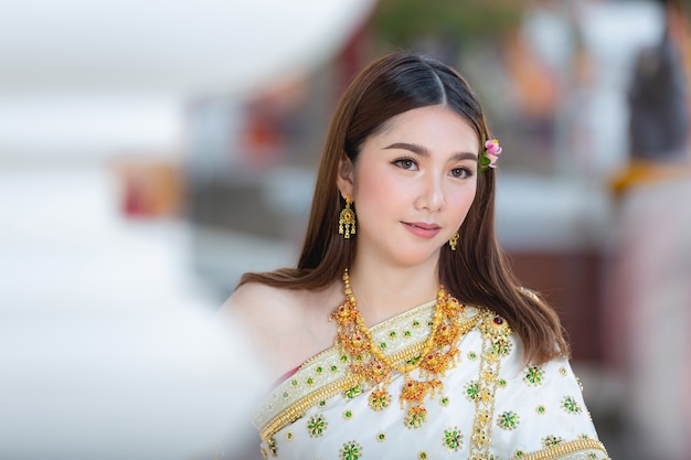 Mooie vrouw die in Thaise traditionele uitrusting en zich bij tempel glimlacht bevindt