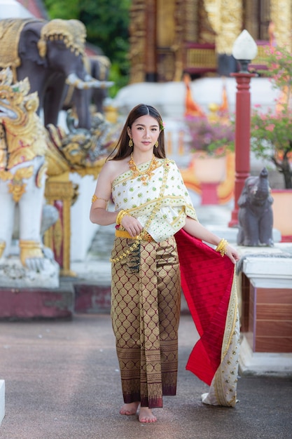 Mooie vrouw die in Thaise traditionele uitrusting en zich bij tempel glimlacht bevindt