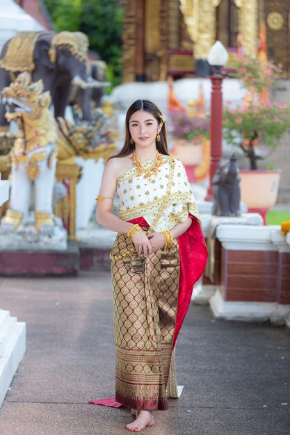 Mooie vrouw die in Thaise traditionele uitrusting en zich bij tempel glimlacht bevindt