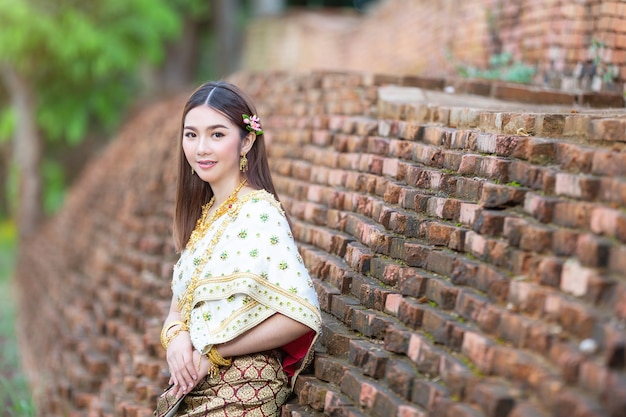 Mooie vrouw die in thaise traditionele uitrusting en zich bij tempel glimlacht bevindt