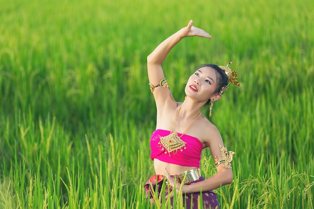 Gratis foto mooie vrouw die in thaise traditionele uitrusting en zich bij tempel glimlacht bevindt