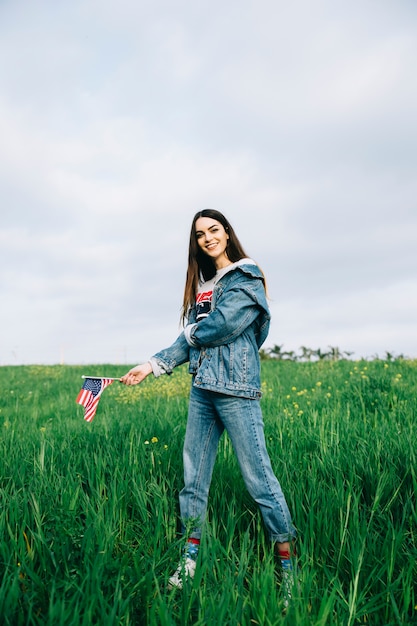 Gratis foto mooie vrouw die in vrijetijdskleding op gras met kleine vlag blijft