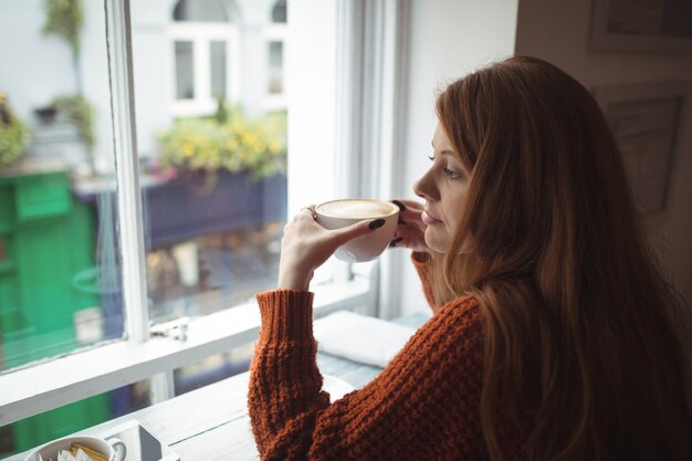 Mooie vrouw die koffie heeft bij venster