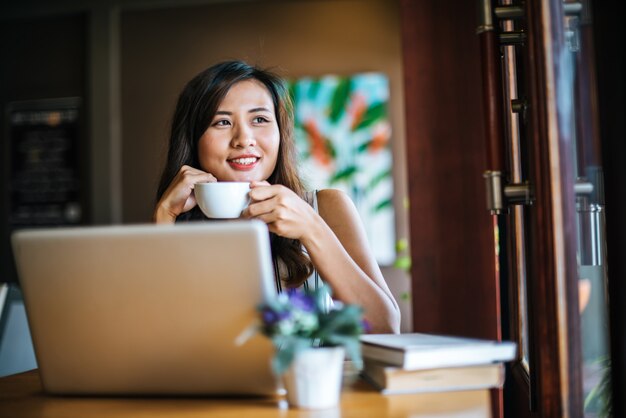 Mooie vrouw die met laptop computer bij koffiewinkelkoffie werkt