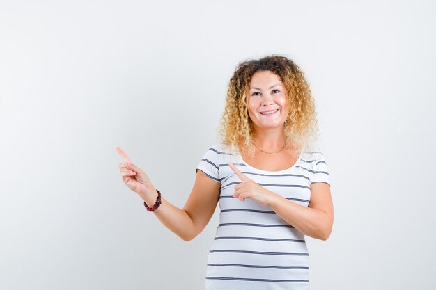 Mooie vrouw die naar de linkerbovenhoek in t-shirt wijst en er vrolijk uitziet, vooraanzicht.