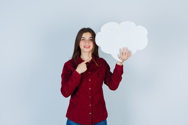 Mooie vrouw die naar de tekstballon wijst terwijl ze lacht in een bordeauxrode blouse en er joviaal uitziet