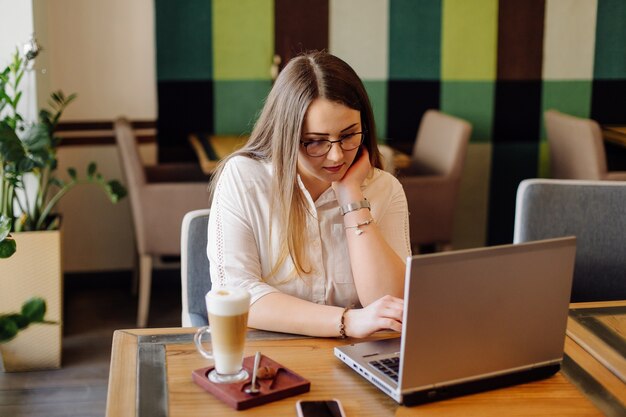 Mooie vrouw die op haar laptop en telefoon aan een stijlvol stedelijk restaurant werkt