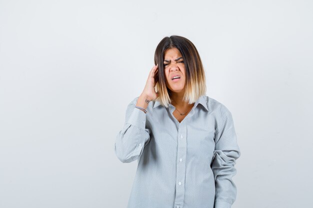 Mooie vrouw die over de slapen wrijft, hoofdpijn in het shirt voelt en er verdrietig uitziet, vooraanzicht.