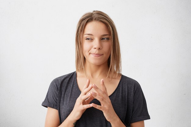 Mooie vrouw die sluw en op mysterieuze wijze opzij kijkt, hand in hand samen met haar lip gebogen met enkele ideeën in haar hoofd.