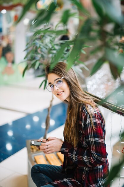 Mooie vrouw die smartphone op bank in winkelcomplex gebruiken