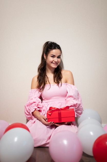 Gratis foto mooie vrouw die valentijnsdag viert in een roze jurk met ballonnen en cadeau