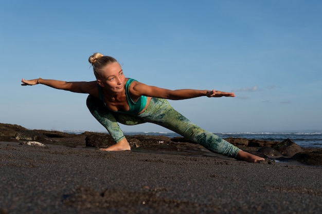 Gratis foto mooie vrouw die yoga op het strand doet