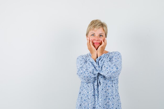 Mooie vrouw hand in hand op haar wangen in blouse met patroon en op zoek glamoureus. vooraanzicht. vrije ruimte voor uw tekst