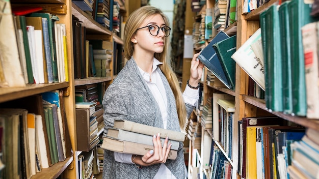 Mooie vrouw het plukken boeken in bibliotheek