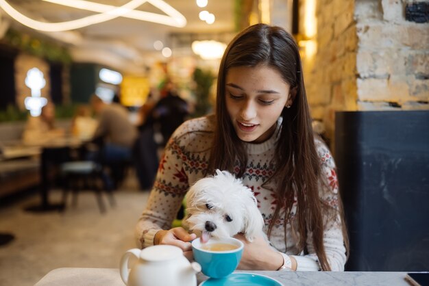 Mooie vrouw houdt haar schattige hond vast, drinkt koffie en lacht in café