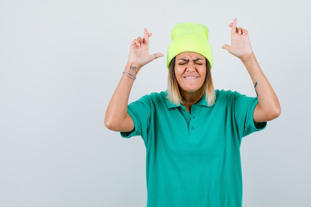 Mooie vrouw houdt vingers gekruist in polo t-shirt, muts en ziet er gelukkig uit, vooraanzicht.