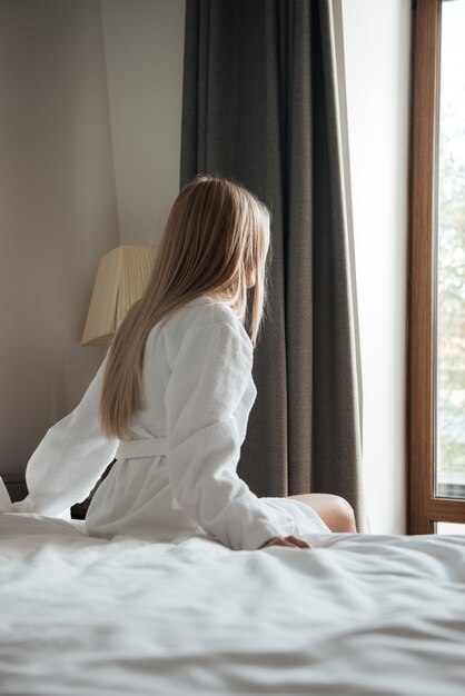 Mooie vrouw in badjas zittend op bed in het hotel