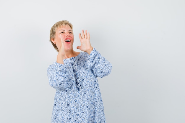 Mooie vrouw in blouse met patroon die iemand met luide stem belt en ongeduldig kijkt, vooraanzicht.