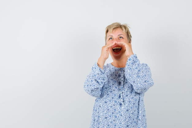 Mooie vrouw in blouse met patroon die onder haar gecombineerde handen schreeuwt en vreugdevol, vooraanzicht kijkt.