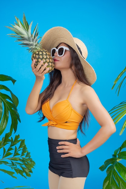 Mooie vrouw in een zwempak die een ananas op blauw houdt