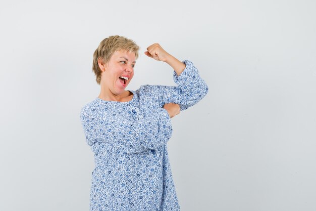 Mooie vrouw in gedessineerde blouse die haar armkracht toont en zelfvoldaan kijkt, vooraanzicht.