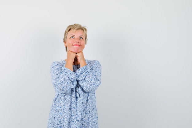 Mooie vrouw in gedessineerde blouse die op haar vuisten leunt en wenselijk, vooraanzicht kijkt. ruimte voor tekst