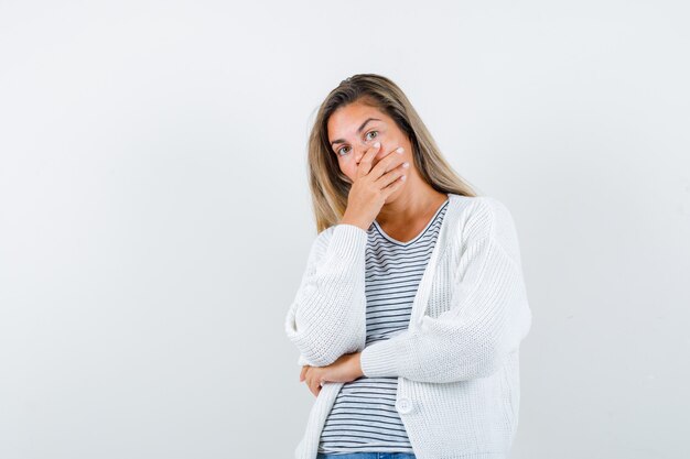 Mooie vrouw in jas die mond behandelt met hand en geschokt, vooraanzicht kijkt.