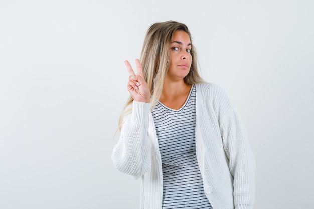 Mooie vrouw in jasje dat V-teken gebaar toont en schattig, vooraanzicht kijkt.