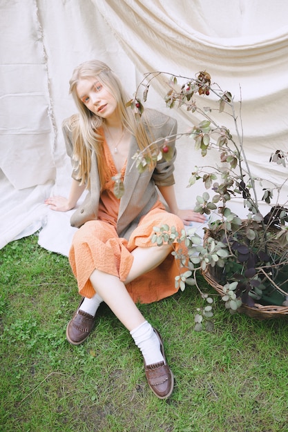 Mooie vrouw in oranje kleding en jasjezitting ter plaatse en kijkend in tuin.