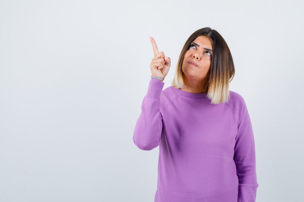 Mooie vrouw in paarse trui die naar de linkerbovenhoek wijst en er gefocust uitziet, vooraanzicht.