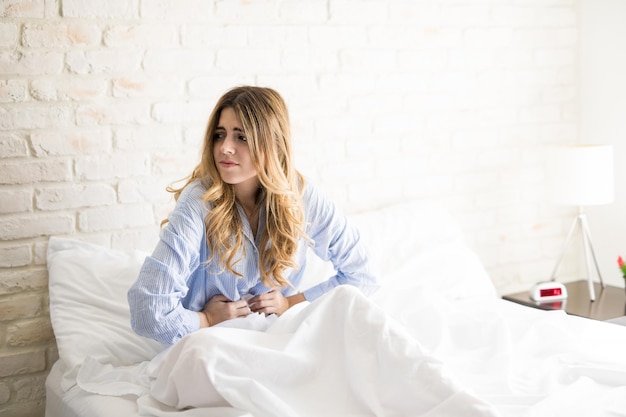 Mooie vrouw in pyjama die zich onwel voelt en last heeft van menstruatiekrampen in haar bed