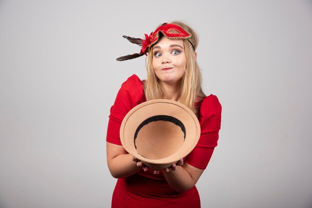 Mooie vrouw in rode jurk die haar hoed aanbiedt.