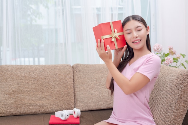 Mooie vrouw in roze jurk, zittend op de bank, het openen van een geschenkdoos.