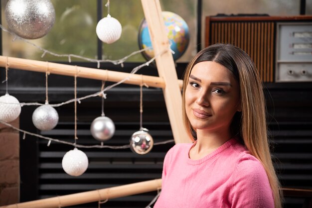 Mooie vrouw in roze trui poseren over kerstverlichting.